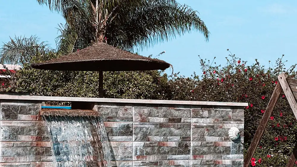 A rock waterfall wall spilling into a pool beside palms