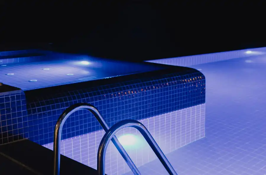 A blue-tiled pool lit at night with a steel handrail