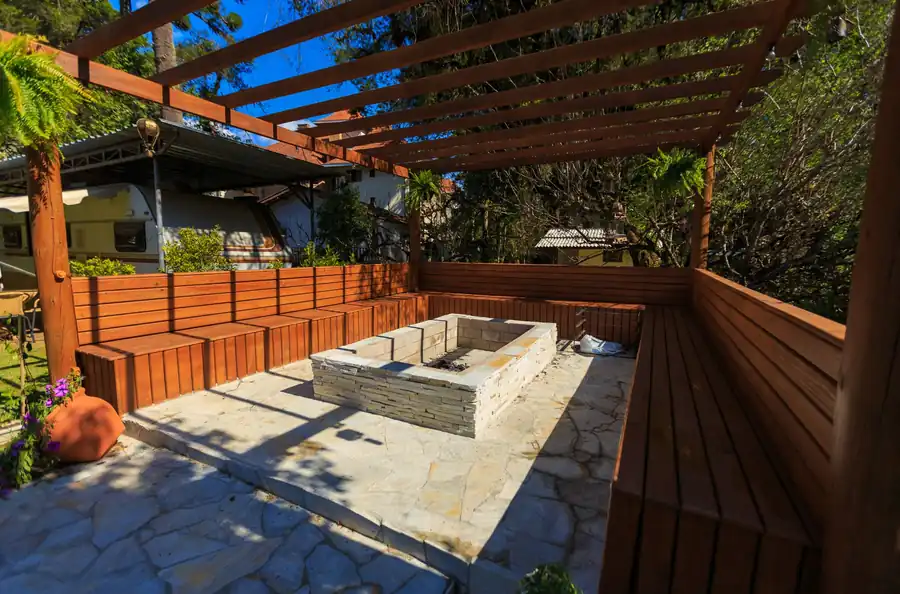 Patio with a stone fire pit and wooden benches under a pergola