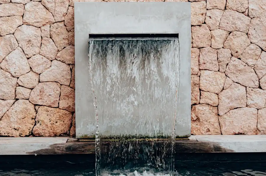 A wide waterfall spout set into a stone wall above a pool