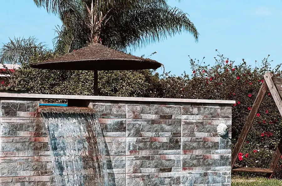 A rock waterfall wall spilling into a pool beside palms