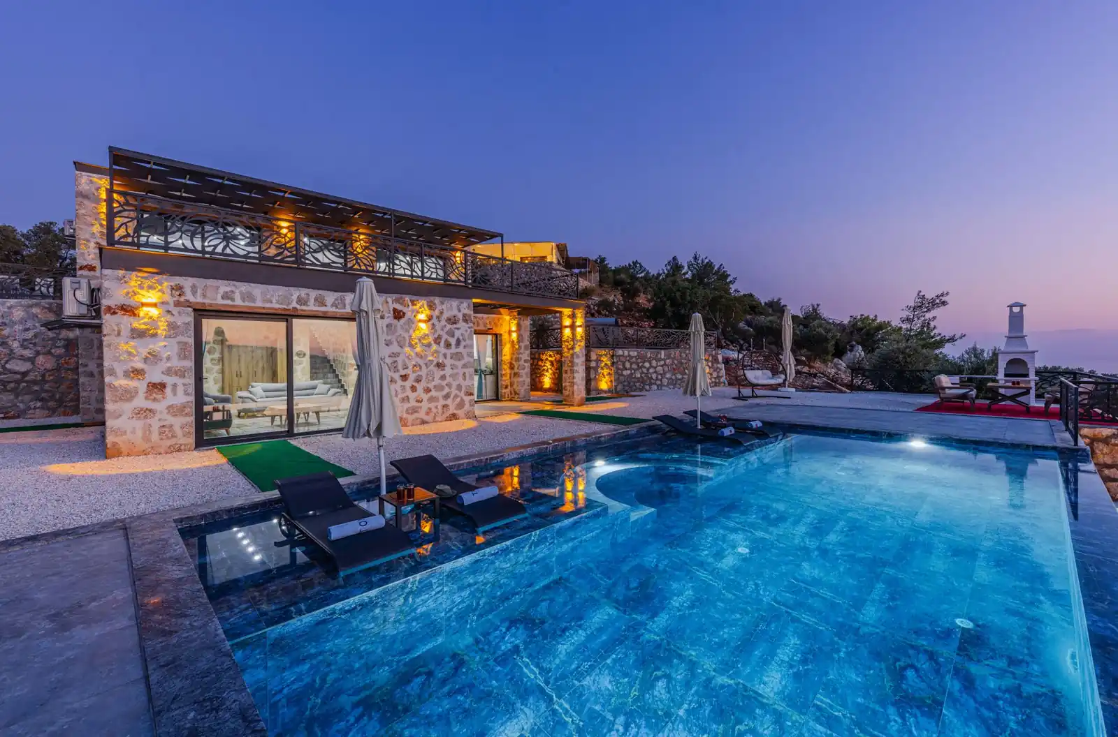 A stone-clad house with a lit swimming pool at twilight