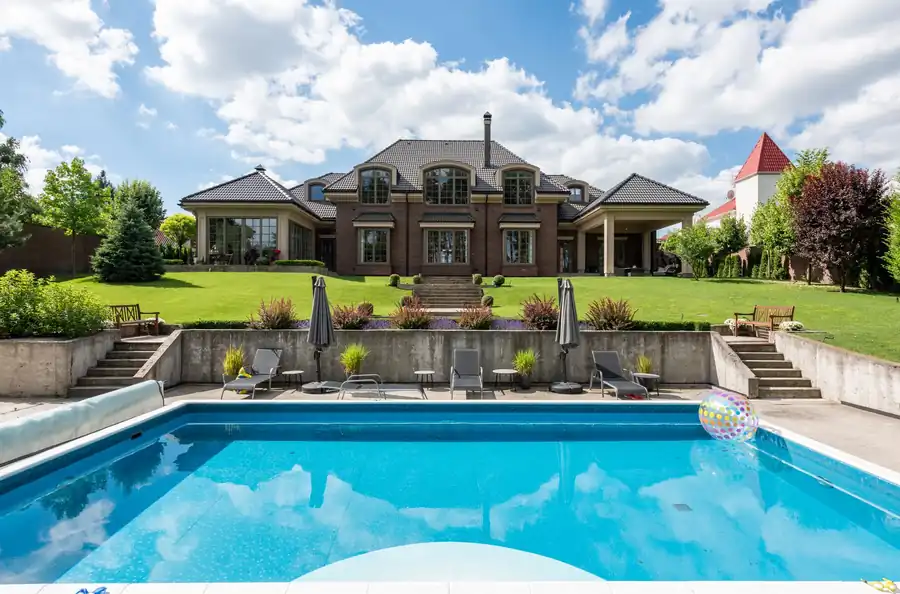 A large home with a pool, umbrellas and manicured garden